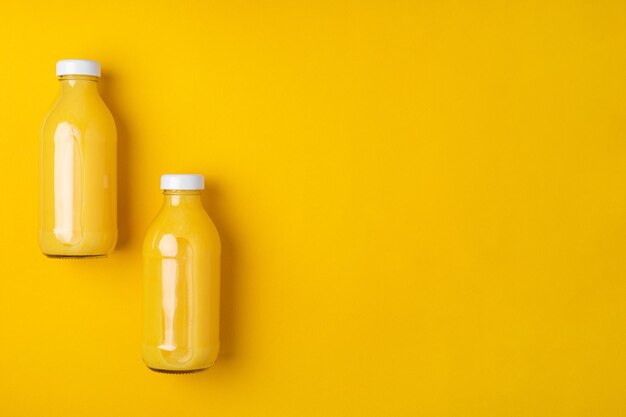 Photo two glass bottles with orange juice on a bright yellow background