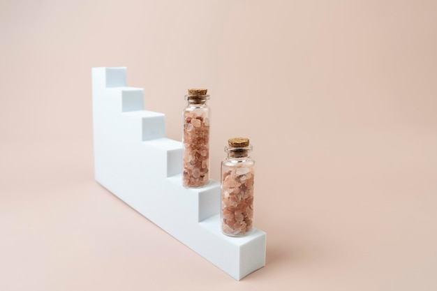 Two glass bottles with pink salt for spa procedures standing on a white stairs