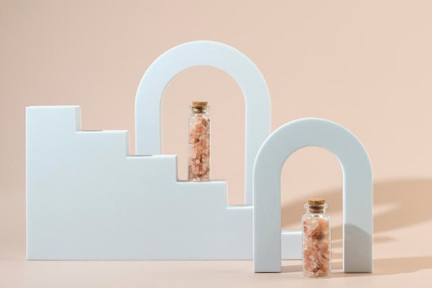 Two glass bottles with pink sea salt for spa procedures for face or body standing between geometric forms