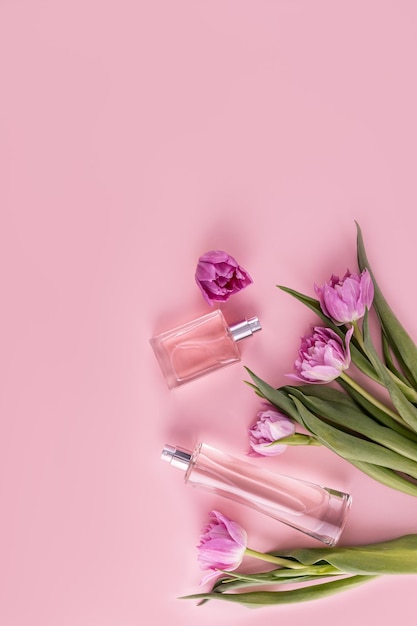 Two glass different bottles with cosmetic spray or perfume on a pink background among tulips Vertical top view Flat lay A copy space