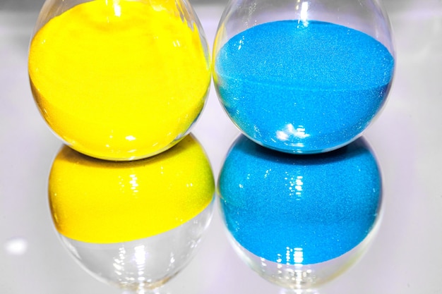 Two glass hourglass flasks containing yellow and blue sand