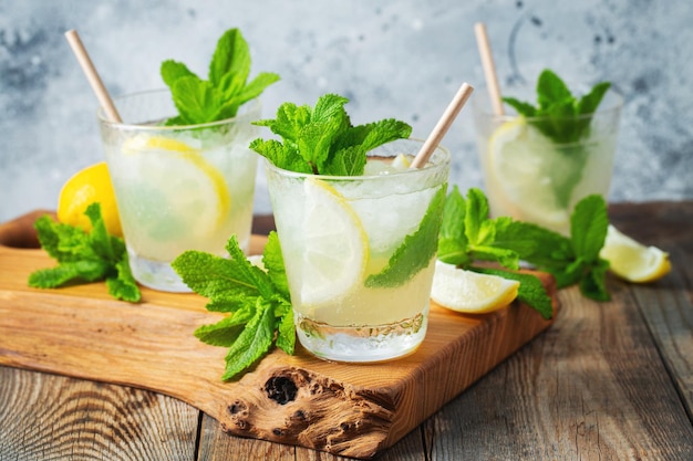 Two glass with lemonade or mojito cocktail with lemon and mint cold refreshing drink or beverage with ice on rustic blue background