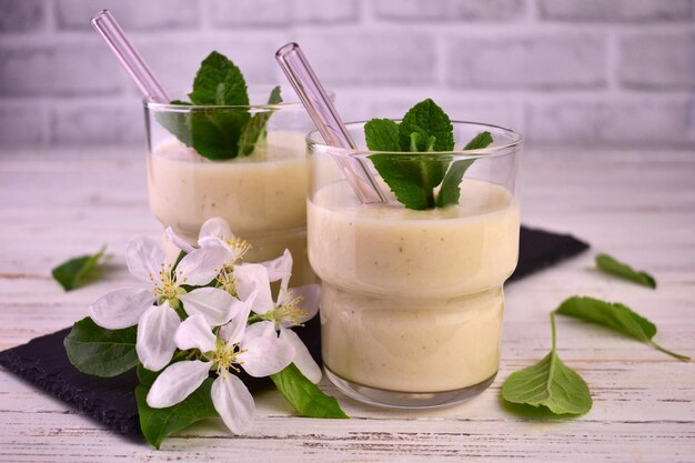 Two glasses of apple and banana smoothie on a white wooden background