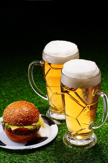 Two glasses of beer and hamburger on green grass