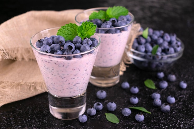 Two glasses of blueberry yogurt with blueberries on a black background