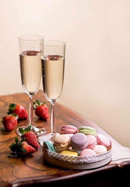 Two glasses of champagne and macarons with strawberries on a wooden table