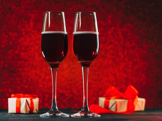 Two glasses of champagne or sparkling wine on a red bokeh background. Gift boxes with red ribbon. The concept of a holiday, Valentine's day or anniversary