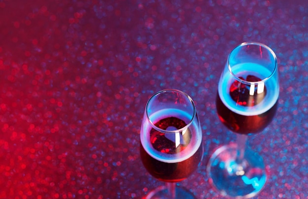 Two glasses of champagne or sparkling wine on a red and neon bokeh background. Top view, copy space and selective focus