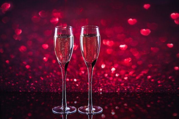 Two glasses of champagne with red heart shape bokeh on background. Romantic dinner. Happy Valentine's day concept.