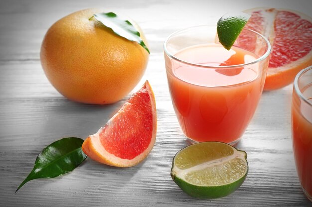 Two glasses of citrus juice and fresh fruits on light wooden background