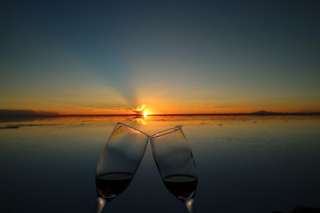 Two glasses clinking to celebrate at the sunset on the mirror effect of Uyuni Salt Flats, 