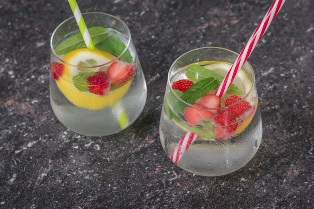 Two glasses of cold water with berries lemon and mint