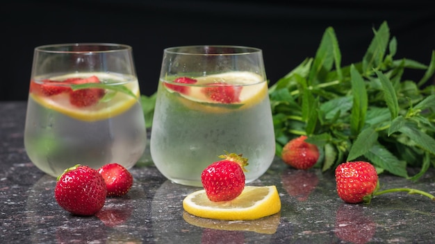 Two glasses of cold water with berries and lemon on a stone background