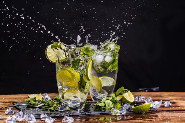 Two glasses of cool mojito on wooden table on black background