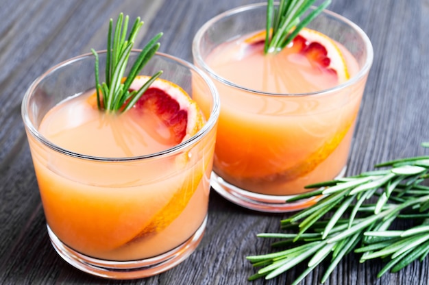 Two glasses of fresh summer drink with blood orange and rosemary on a dark wooden background