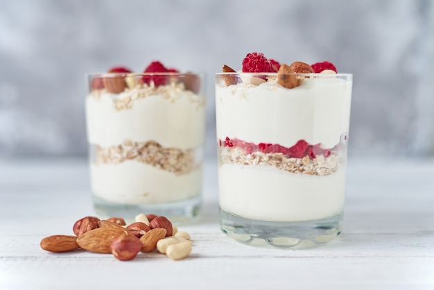 Two glasses of greek yogurt granola with raspberries, oatmeal flakes and nuts on a white background. Healthy nutrition