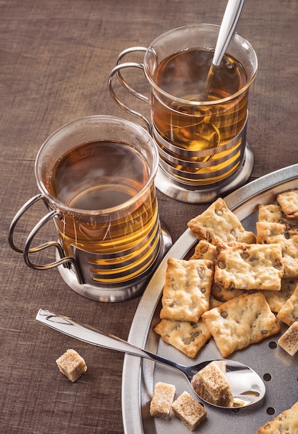 Two glasses of hot tea and biscuits Lumps of brown sugar on dark table