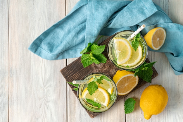 Two glasses of lemonade, lemons and mint on a light background. Top view, copy space.