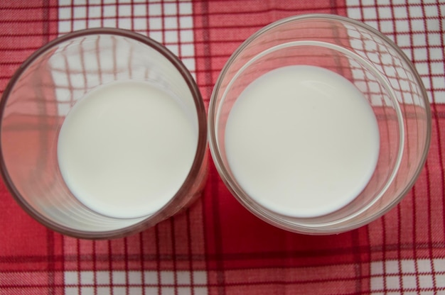 Two glasses of milk stand on a red checkered cloth top view