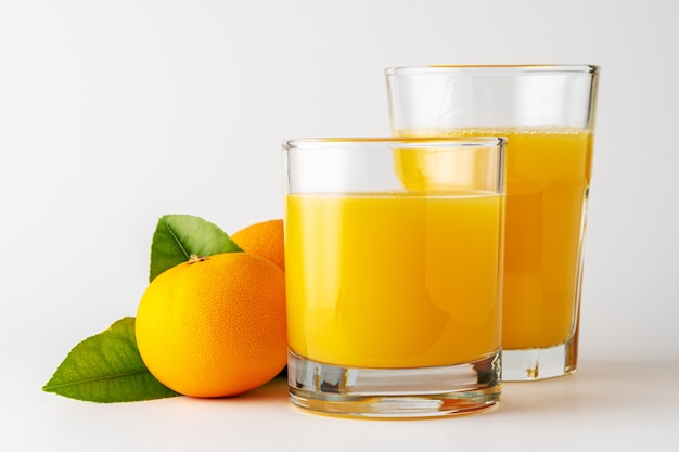 Two glasses of orange juice on white wall.