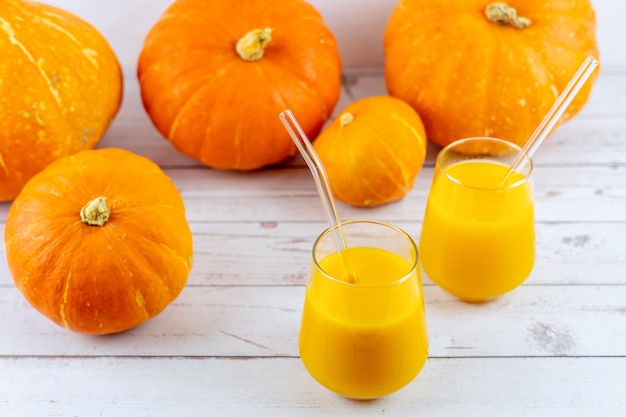 Two glasses of pumpkin juice with fresh pumpkins on a wooden table