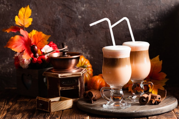 Two glasses pumpkin spicy latte with whipped cream and cinnamon on a wooden stand