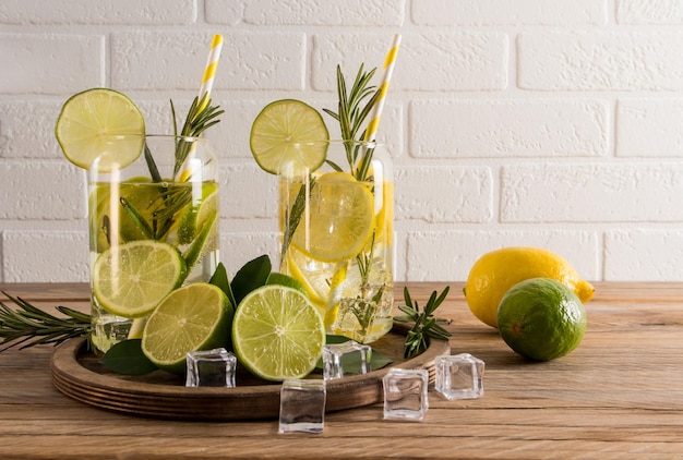 Two glasses of refreshing citrus water a cocktail or tonic with ice cubes on a wooden table against a white brick wall useful detox