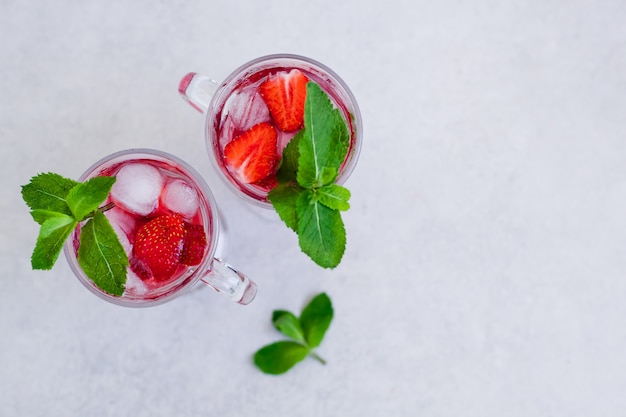 Two glasses of summer strawberry drink with mint on a light background