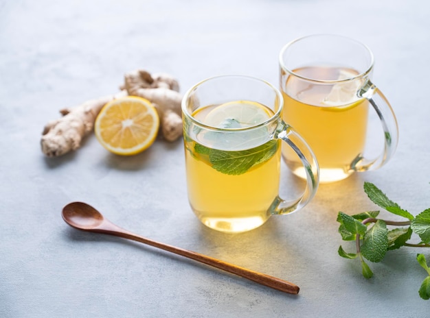 Two glasses of tea with fresh lemon mint and ginger on a light background with morning light The concept of a healthy drink for immunity