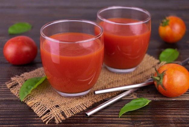 Two glasses of tomato juice on a dark wooden background.