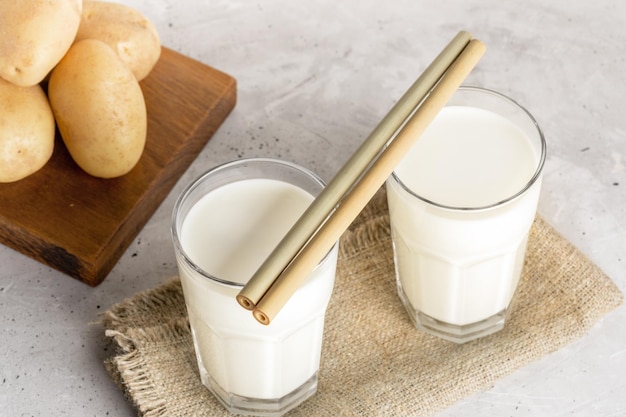 Two glasses of vegan potato milk with bamboo drinking straws close up on neutral background