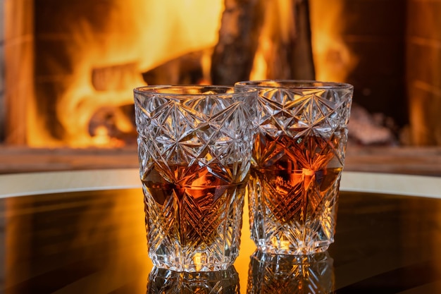 Two glasses of whiskey with ice on a background of a burning fireplace