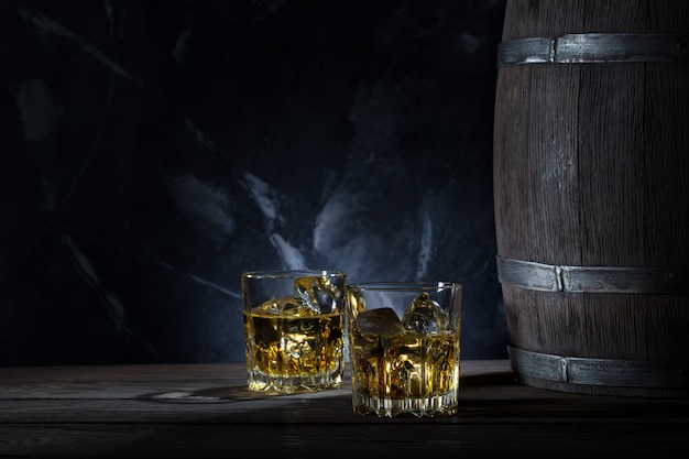 Two glasses of whiskey with ice and wooden barrel