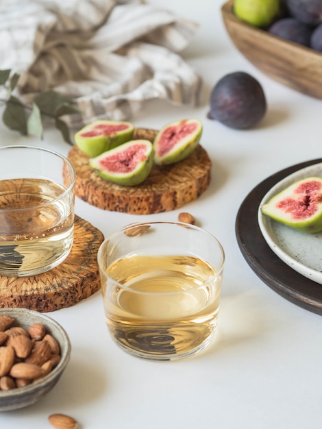 Two glasses of white wine, figs and almonds on a white background. 