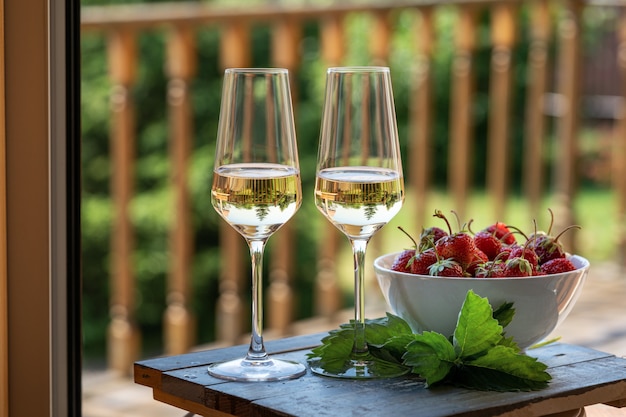 Two Glasses of white wine and strawberry over green garden and country house background.