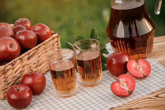 Two glasses with apple juice and basket with apples on wooden table with natural orchard background Vegetarian fruit composition