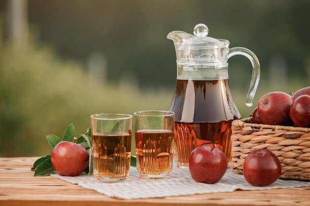 Two glasses with apple juice and basket with apples on wooden table with natural orchard background Vegetarian fruit composition