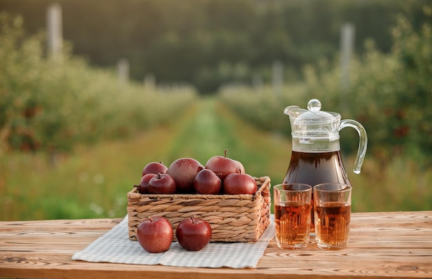 Two glasses with apple juice and basket with apples on wooden table with natural orchard background Vegetarian fruit composition