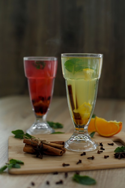 Two glasses with colored hot drinks from which steam comes