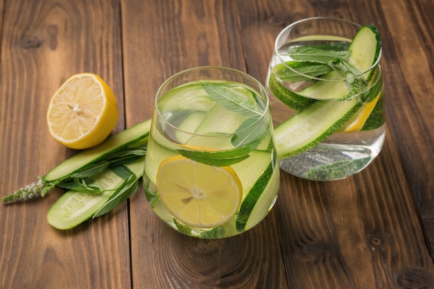 Two glasses with drinks of mint and cucumber with lemon on a wooden table