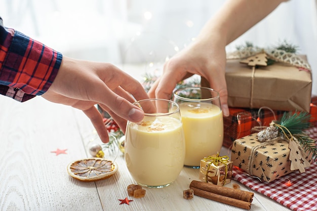 Two glasses with eggnog in hand christmas dessert sweet winter cocktail selective focus