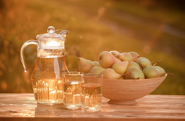 Two glasses with pear juice and basket with pears on wooden table with natural orchard background on sunset light Vegetarian fruit composition