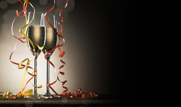 Two glasses with sparkling champagne and decorative ribbons on black background with backlight and copy space