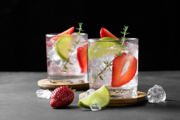 Two glasses with summer strawberry soda drink or mojito with strawberry ice cubes and lime on dark background