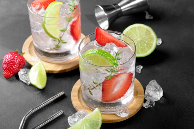 Two glasses with summer strawberry soda drink or mojito with strawberry ice cubes and lime on dark