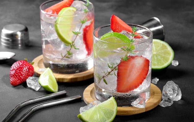 Two glasses with summer strawberry soda drink or mojito with strawberry ice cubes and lime on dark