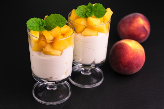 Two glasses of yogurt with peach on a black background.