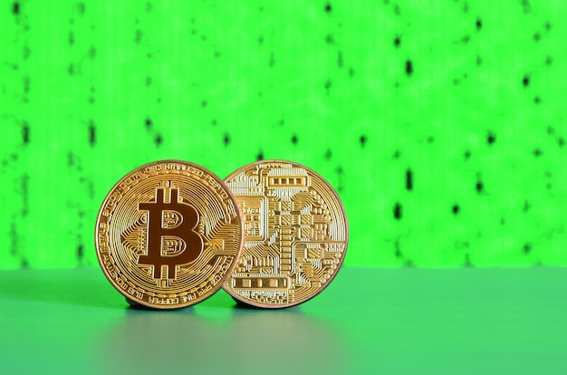 Two gold bitcoins lie on the green surface on the background of the display