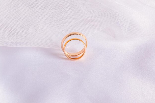 Two gold wedding rings on the background of the white bridal veil and the satin texture of the fabric A copy space The concept of the wedding