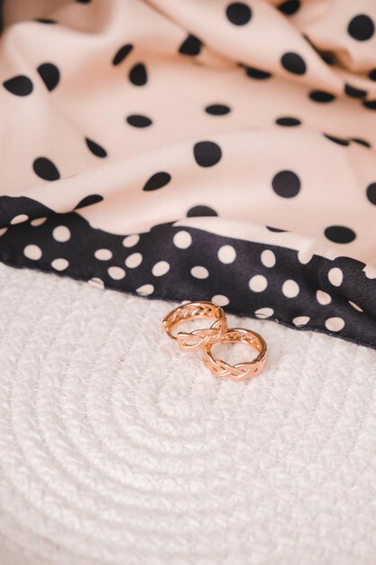 Two gold wedding rings sit on a bed with a polka dot blanket.